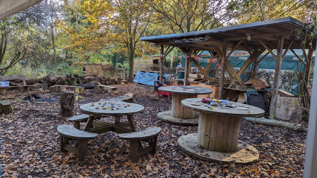 IMG-20241110-WA0008 (1) An image showing the site at Martineau Gardens, with large cable reel tables, a picnic bench laid out with crafts and autumnal leaves.