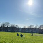 An urban park on a sunny day, with children running off to play